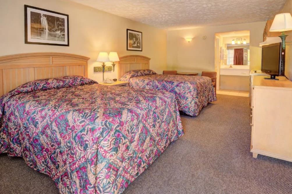 A hotel room with two queen beds, a dresser, and a TV.