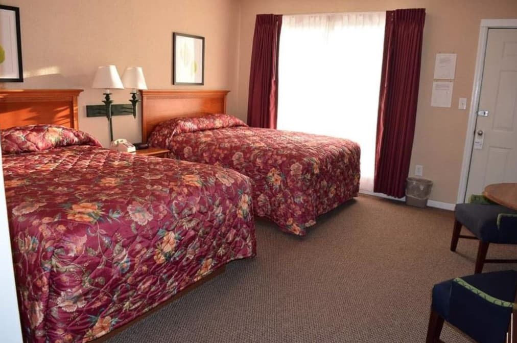 A hotel room with two beds, a window, and a door.